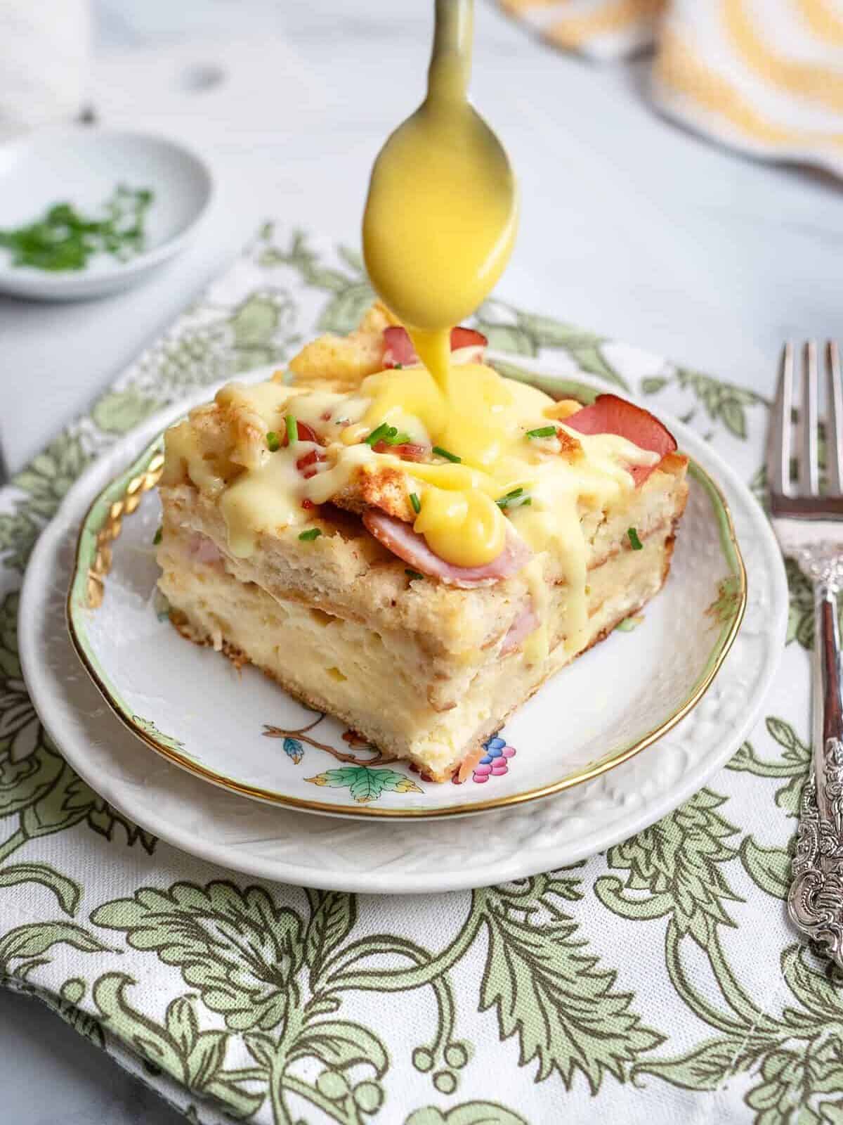 A square slice of eggs benedict casserole for Easter morning brunch and topped with hollandaise sauce and chopped chives.