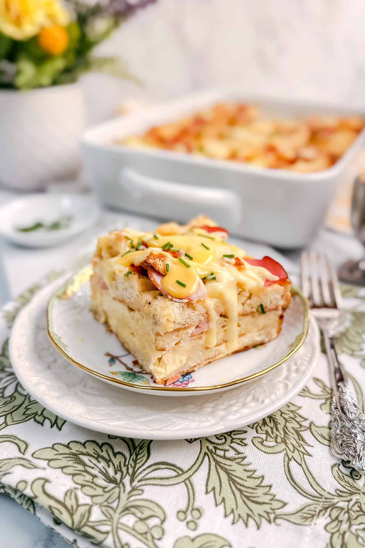 Eggs benedict casserole slice on plate with baking dish in background.
