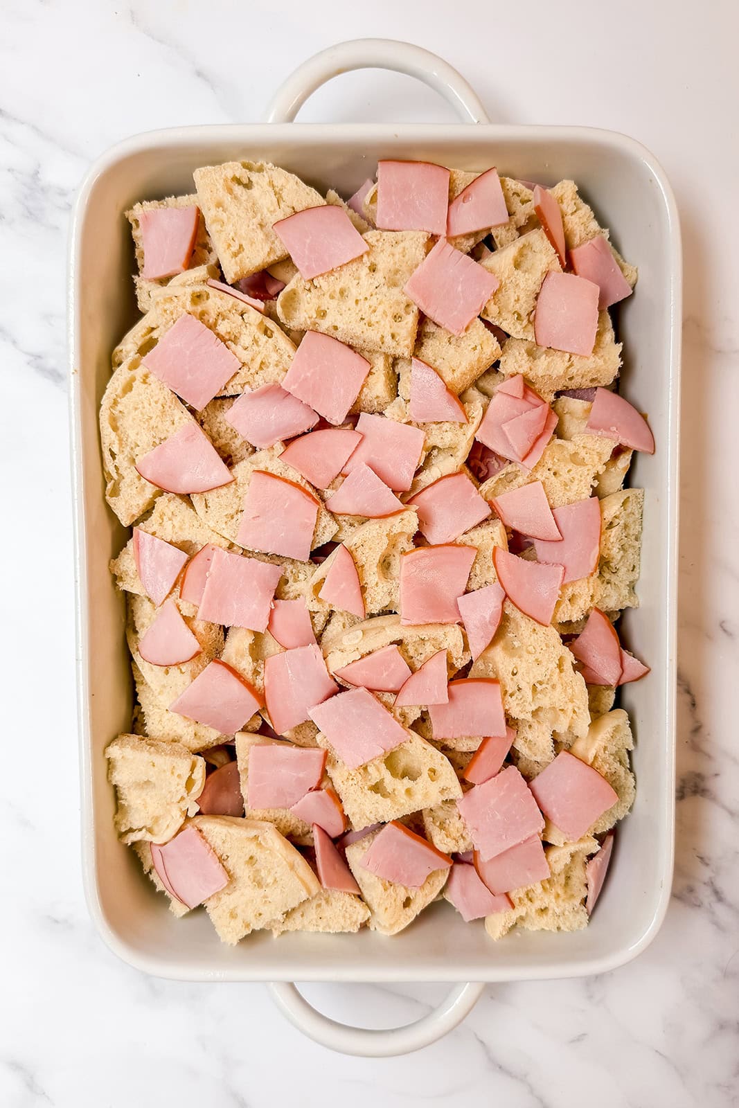 Layering english muffins and canadian bacon in a casserole dish for eggs benedict casserole.