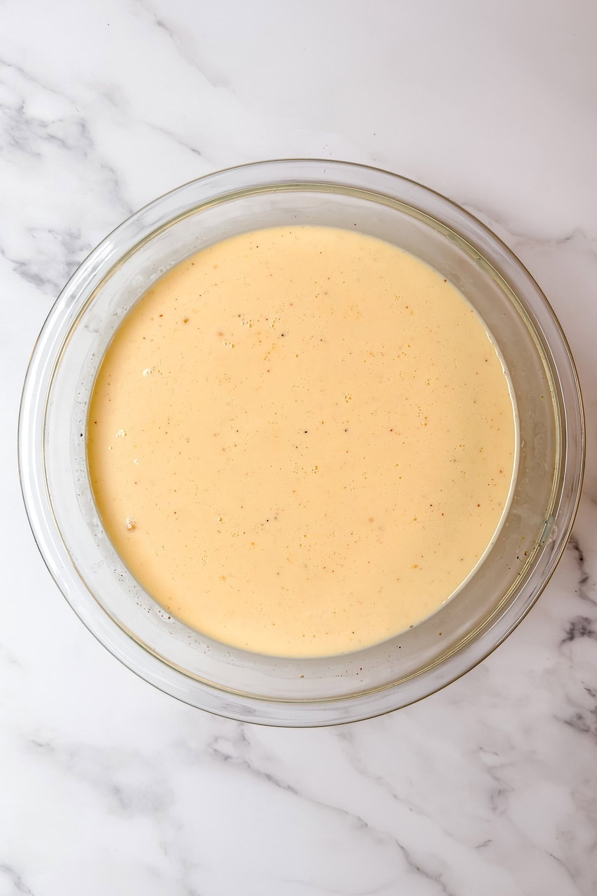 Egg mixture for eggs benedict casserole being whisked in a glass bowl with spices visible.