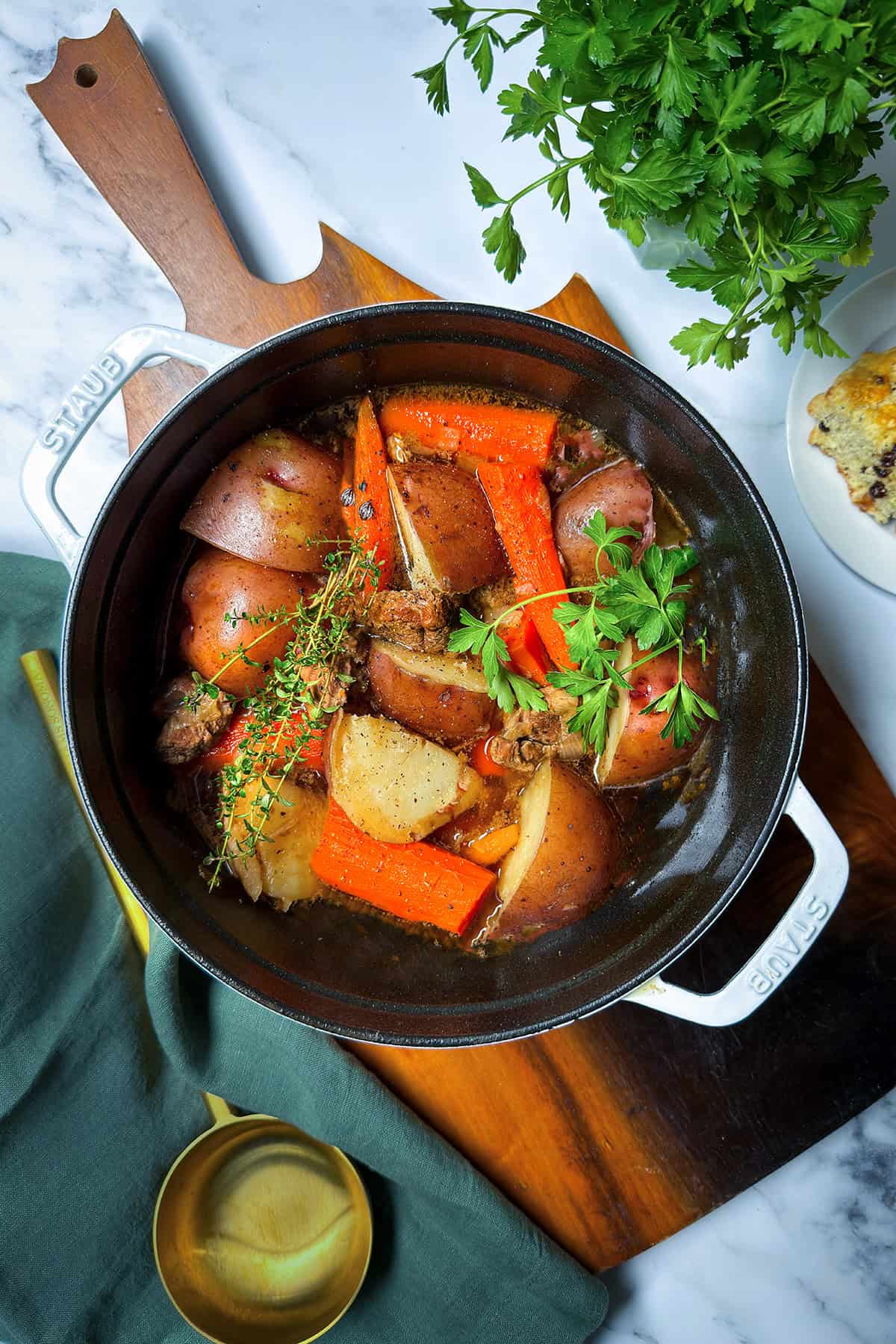 A pot of Irish Stew with chunks of beef, red potatoes, carrots, and herbs sits on a wooden board, garnished with fresh parsley and thyme.