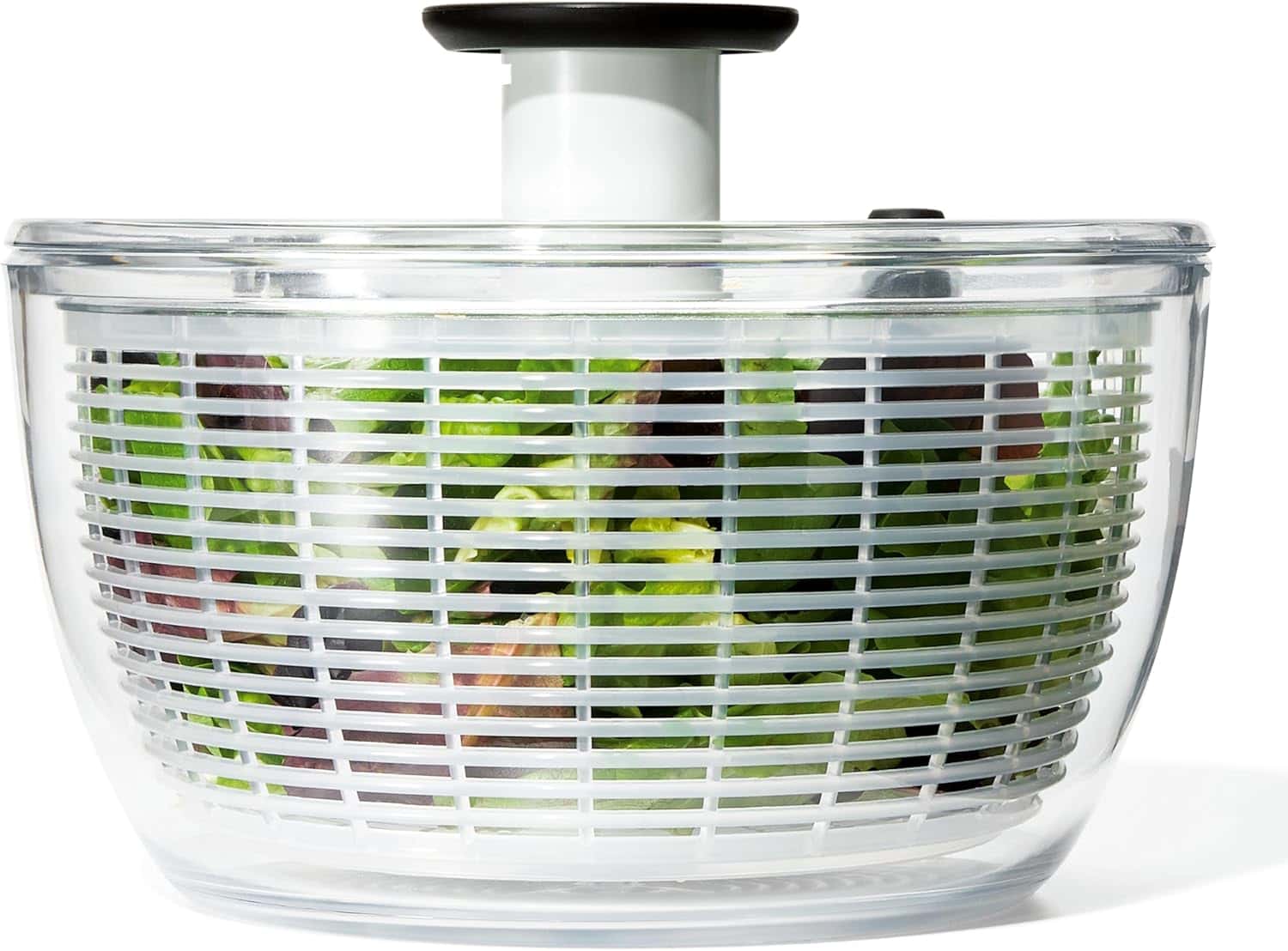 A clear plastic salad spinner with leafy greens inside.