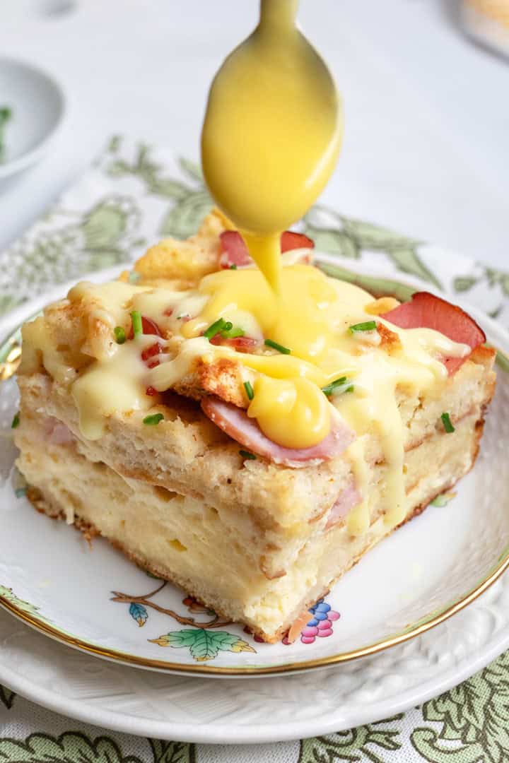 Eggs benedict casserole serving with hollandaise sauce being poured over top.