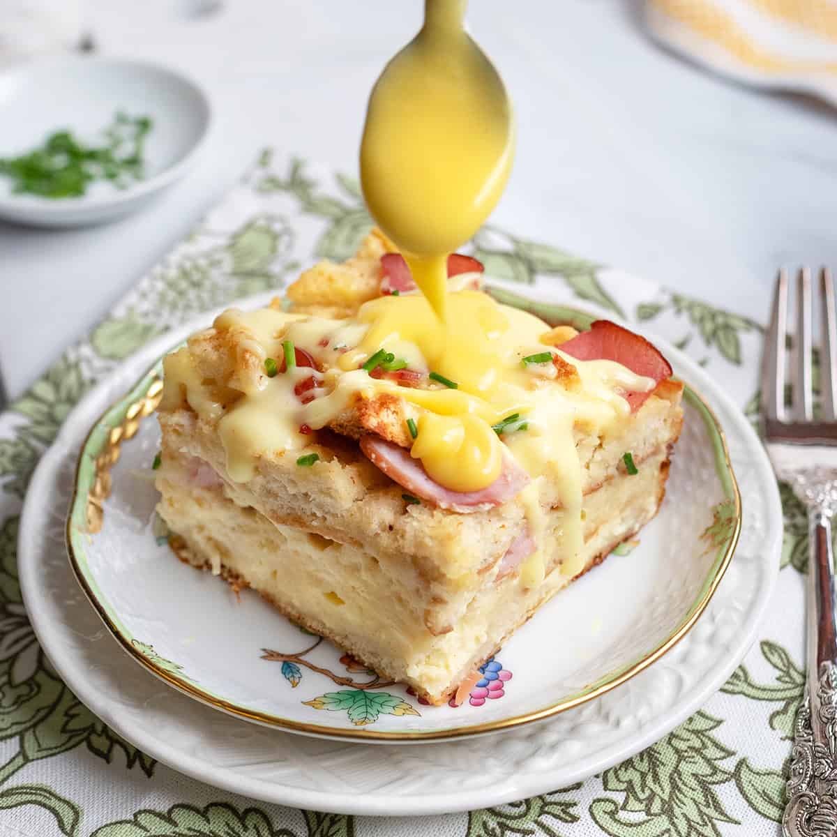 Eggs benedict casserole serving with hollandaise sauce being poured over top.