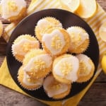 A plate of lemon yogurt muffins with white icing and lemon zest.