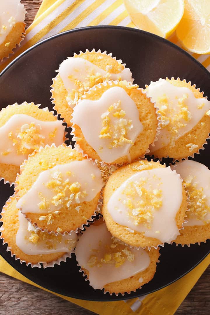 A plate of Greek yogurt lemon muffins with white icing and lemon zest.