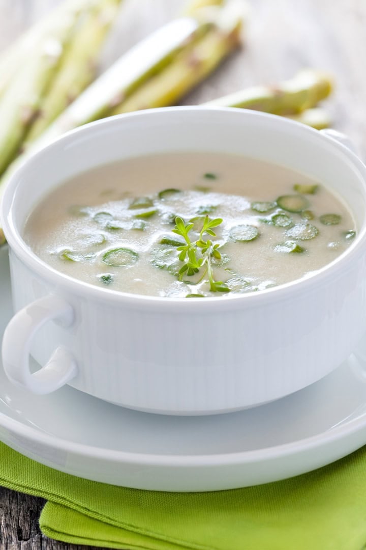 A bowl of creamy asparagus soup garnished with fresh herbs for Stephanie Wilson's Cream of Asparagus Soup.