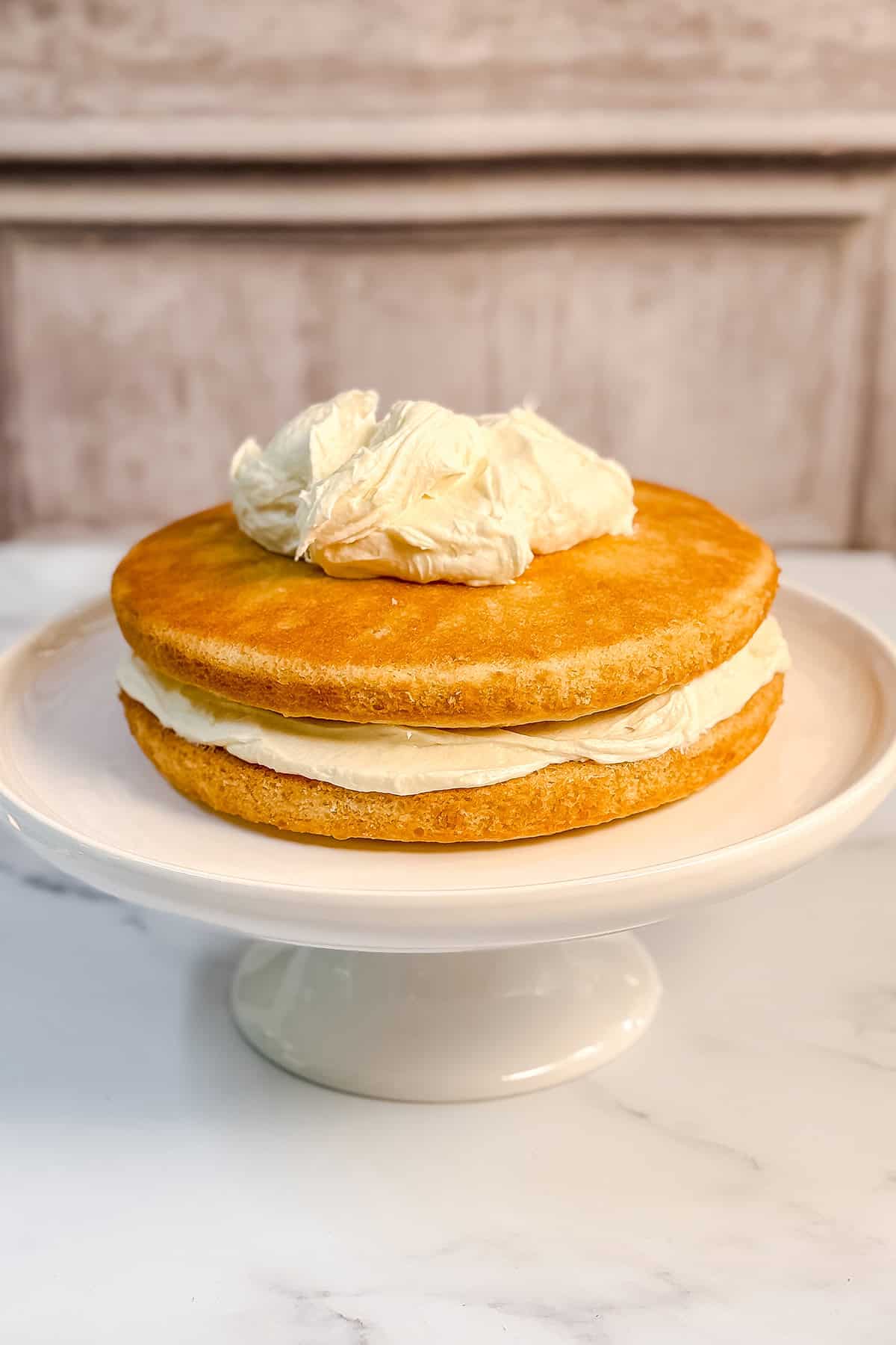 Assembling a coconut cake and spreading coconut cream cheese buttercream frosting between two layers.