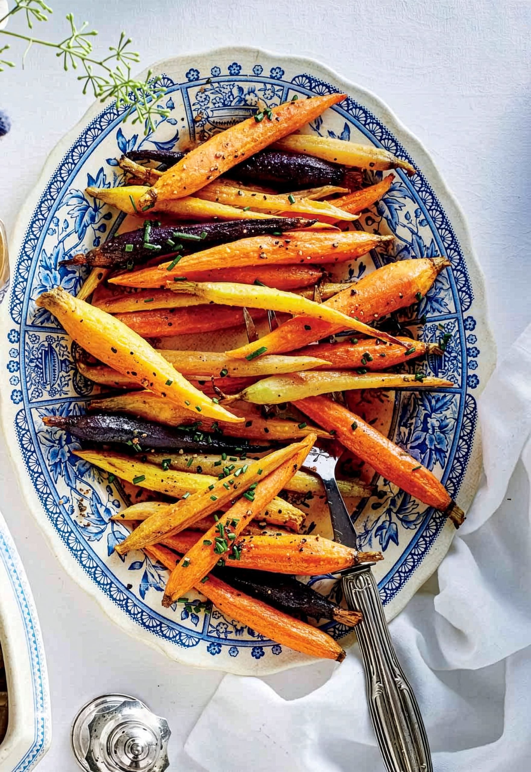 A decorative plate with roasted multicolored carrots, garnished with herbs and black sesame seeds, showcases one of our quick and easy recipes, served on a white table with a fork beside the plate.