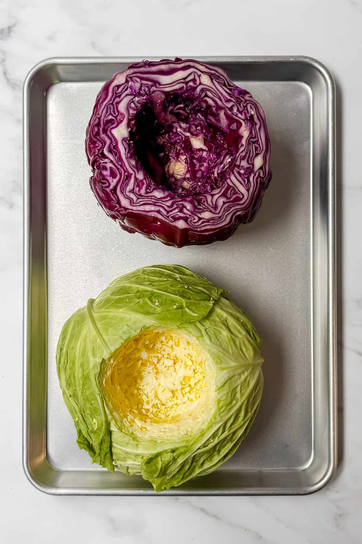 A halved red cabbage and a halved green cabbage are placed cut side up on a metal baking tray, ready to be featured in a vibrant Spring Crudites spread.