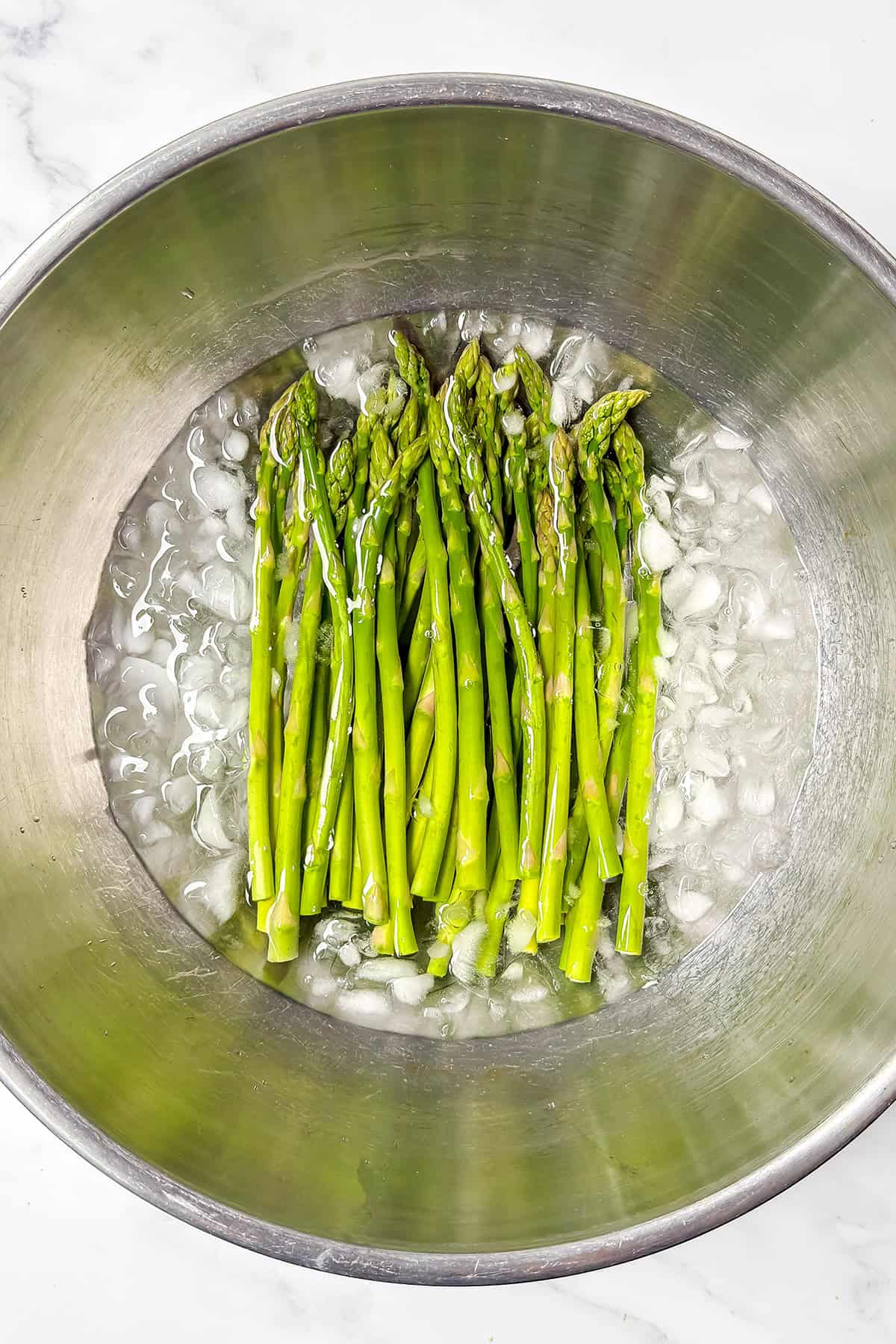 A bunch of blanched spring vegetables, like asparagus spears, cooling in a metal bowl filled with ice water-perfect for adding to your spring crudites platter.