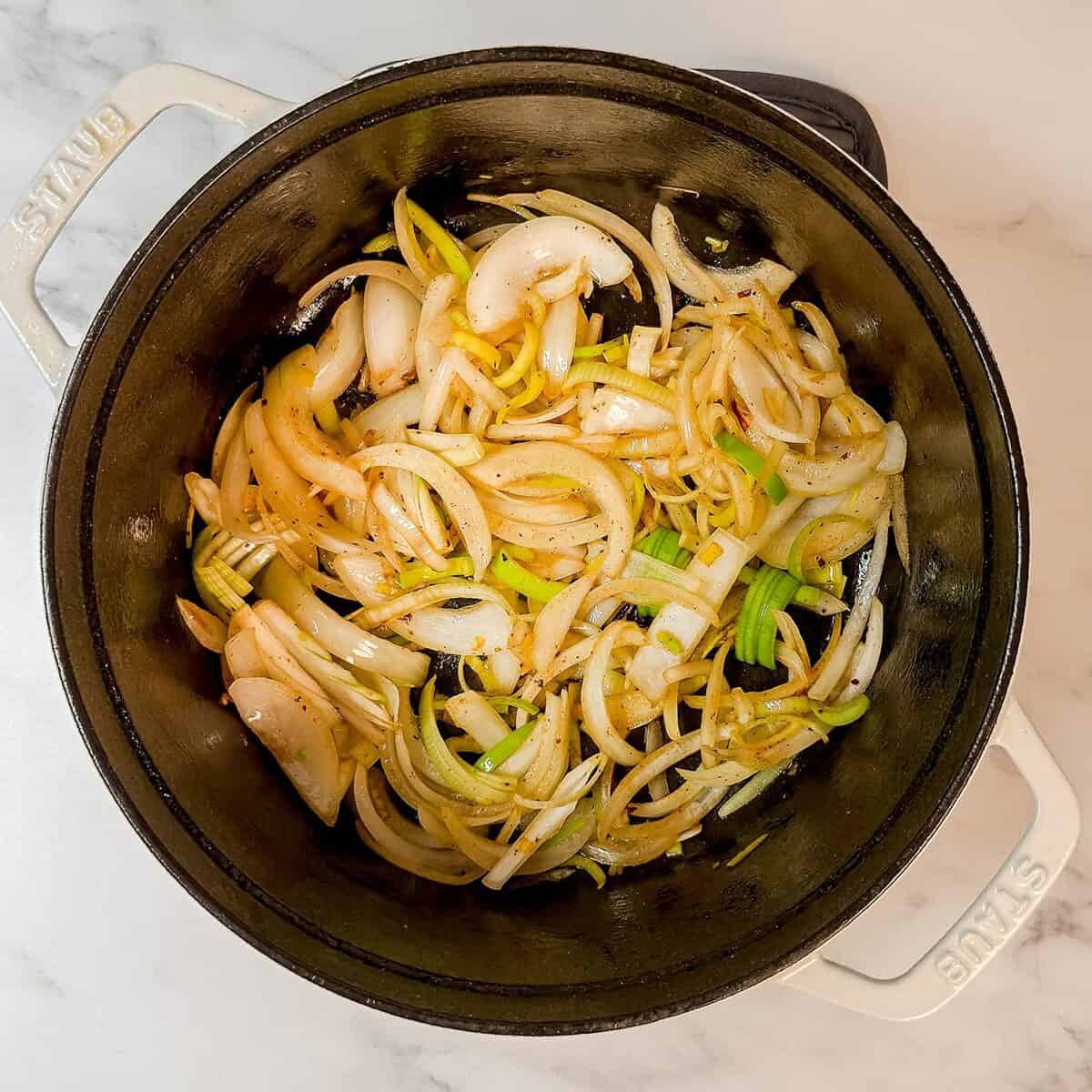 Sliced onions simmering in a white Dutch oven on a marble countertop, perfect for starting a hearty Dublin Coddle.