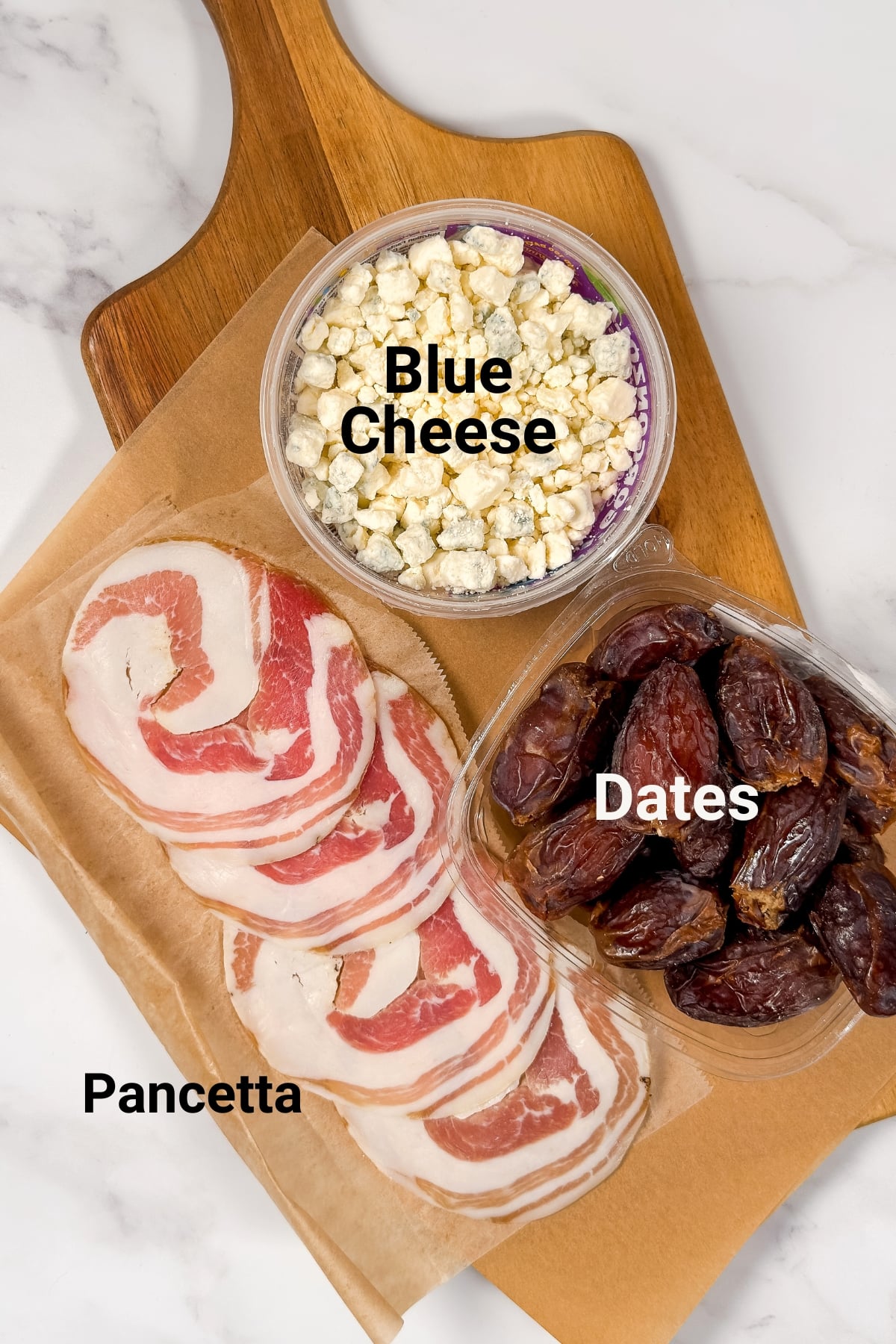 A tempting appetizer featuring blue cheese, pancetta slices, and a container of dates-perfect for crafting stuffed dates-arranged on a wooden board with parchment paper.