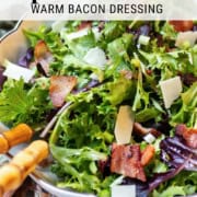 A bowl of spinach salad topped with bacon pieces, shaved cheese, and a warm bacon dressing, served with wooden-handled utensils—a delicious Spinach Salad recipe perfect for any meal.