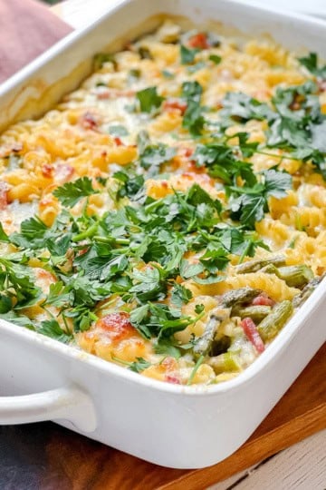 A baked pasta casserole with rotini, asparagus, vegetables, melted cheese, and fresh parsley, served in a white rectangular dish—perfect for main dish asparagus recipes.
