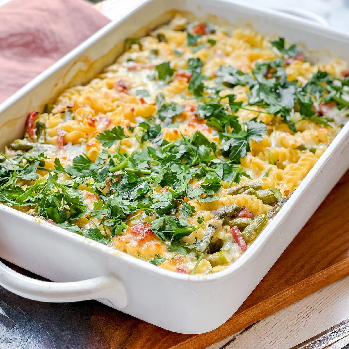 A baked pasta casserole with rotini, asparagus, vegetables, melted cheese, and fresh parsley, served in a white rectangular dish-perfect for main dish asparagus recipes.
