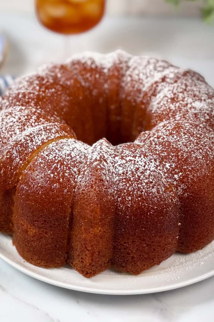 A golden-brown Kentucky Butter Cake dusted with powdered sugar sits on a white plate on a marble surface.
