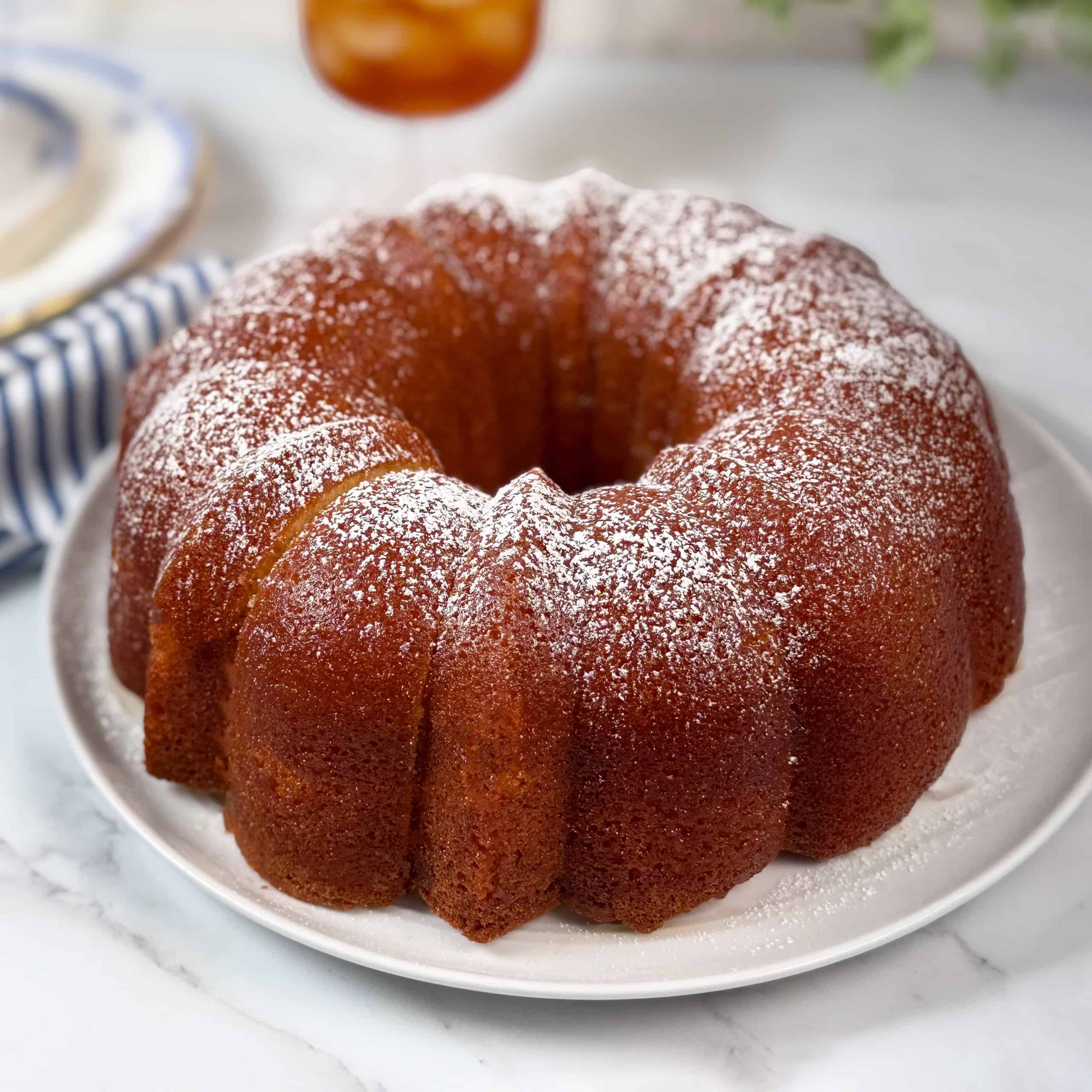 A golden-brown Kentucky Butter Cake dusted with powdered sugar sits on a white plate on a marble surface.