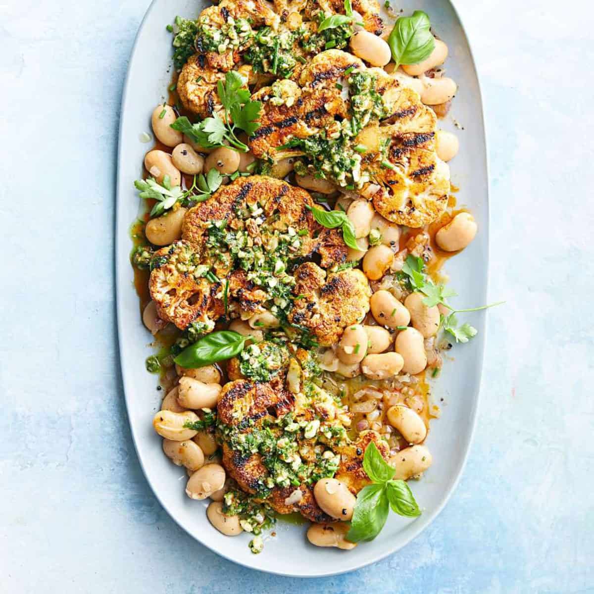 Grilled cauliflower steaks garnished with herbs and sauce, served on a platter with white beans and fresh basil leaves-perfect for light Spring Mediterranean Diet Dinners.