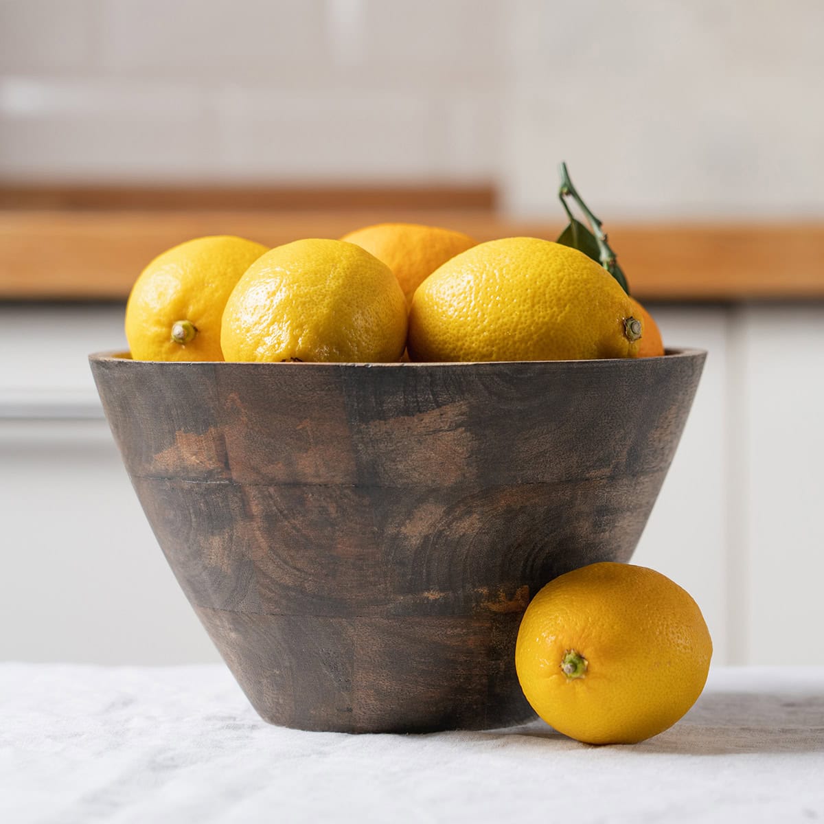 A wooden bowl filled with lemons sits on a white surface for 31Daily's Sunday Edit Spring Garden Table.