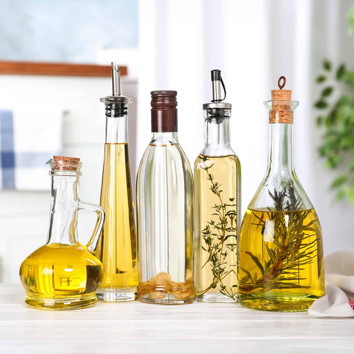 Five glass bottles filled with various oils and herbs are arranged on a light wooden surface, adding a rustic touch to your Easter table, with a blurred kitchen background.