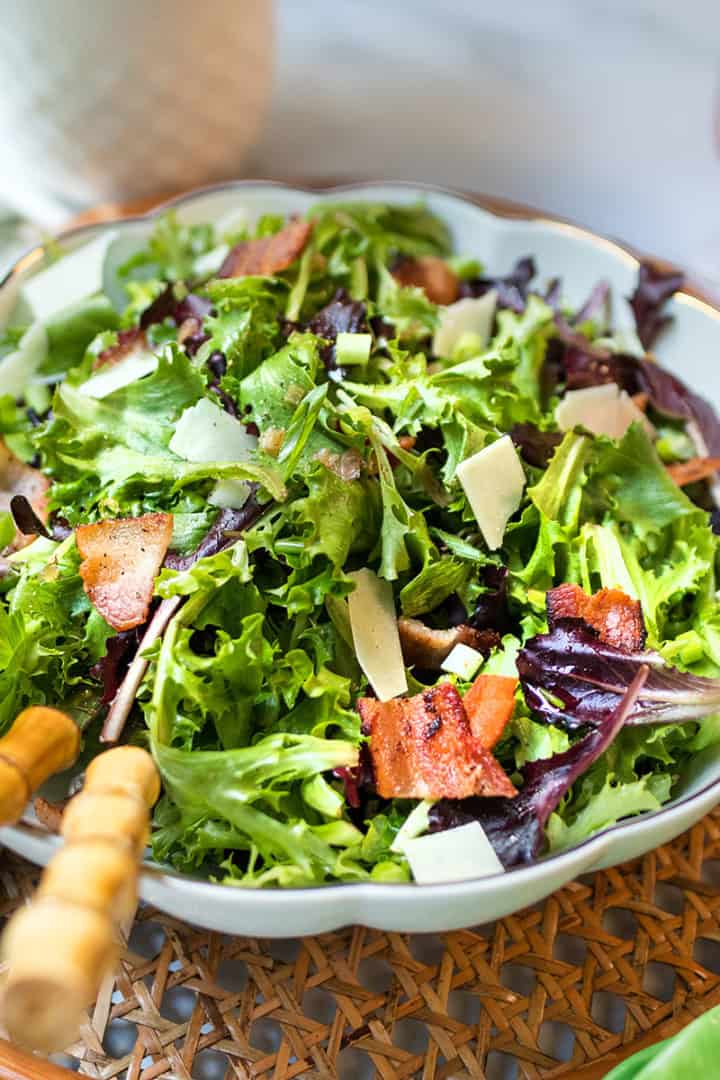 A refreshing Spinach Salad topped with bacon pieces and shaved cheese, served on a woven tray.