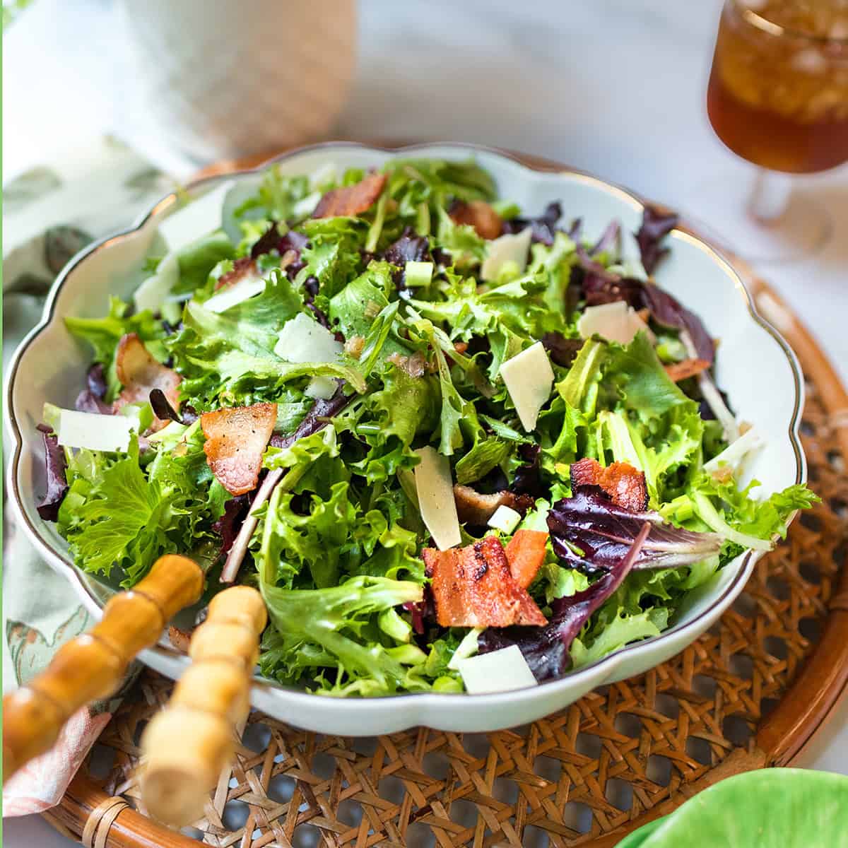 A refreshing Spinach Salad topped with bacon pieces and shaved cheese, served on a woven tray.