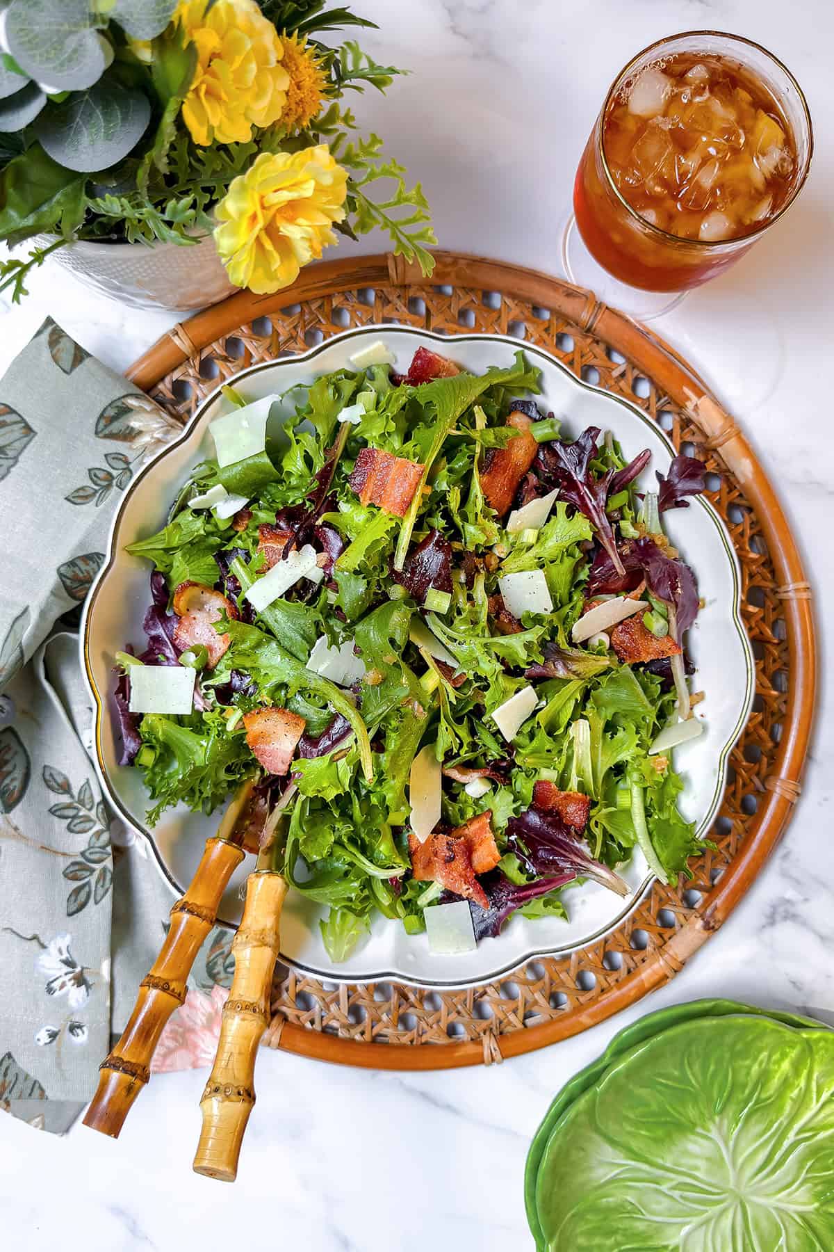 A bowl of mixed green spinach salad with cheese shavings and a warm bacon dressing.