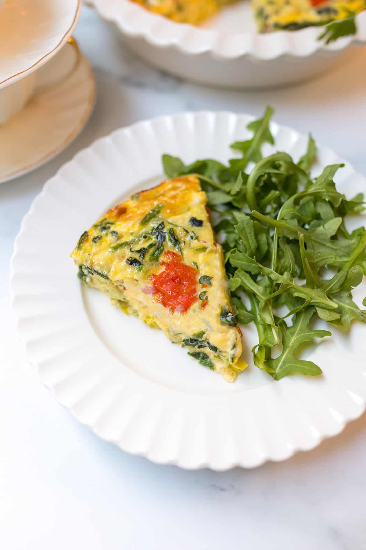 A slice of crustless quiche is served on a white plate alongside a small portion of fresh arugula.