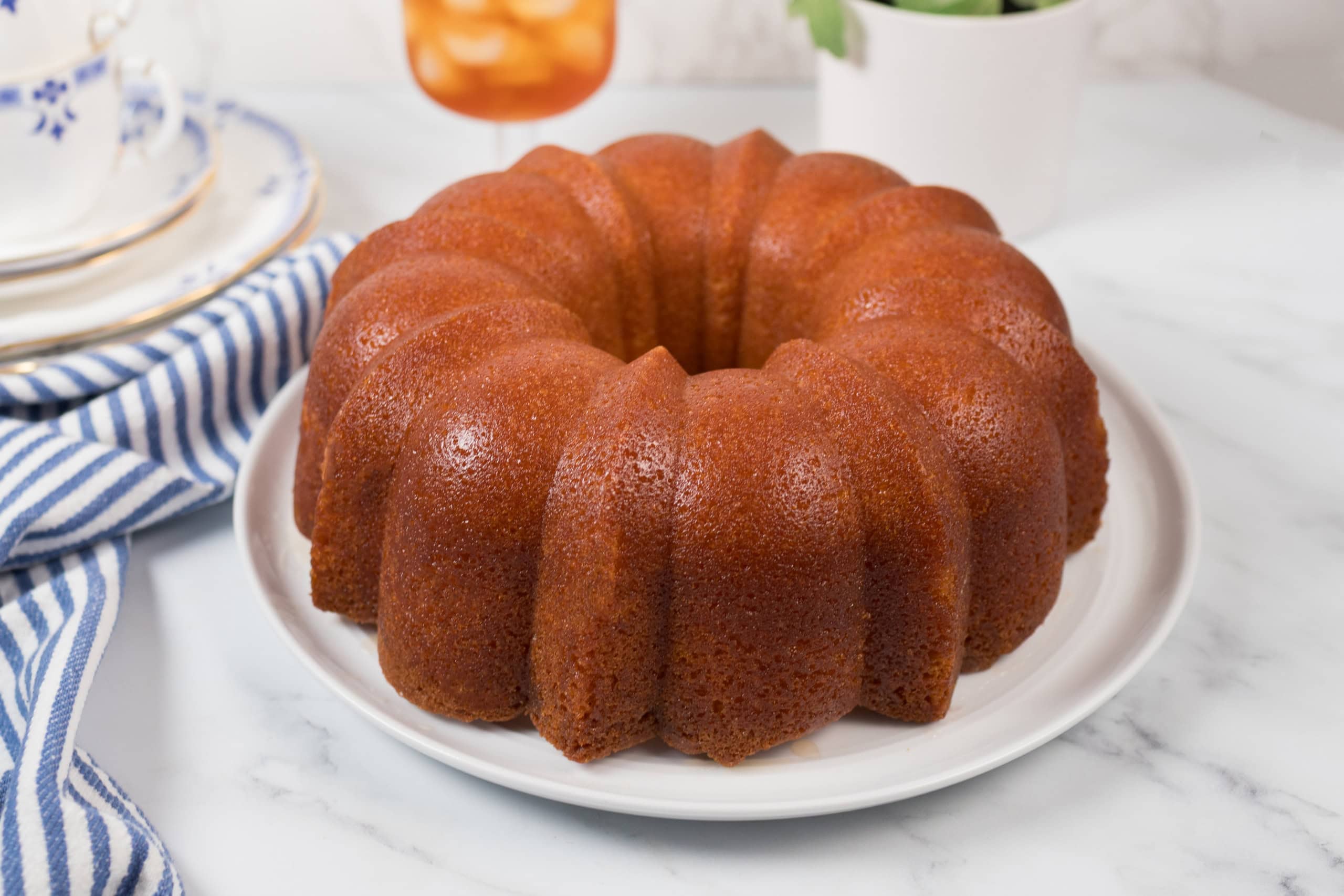 A classic Kentucky Butter Cake sits on a white plate atop a marble surface, with a striped napkin.