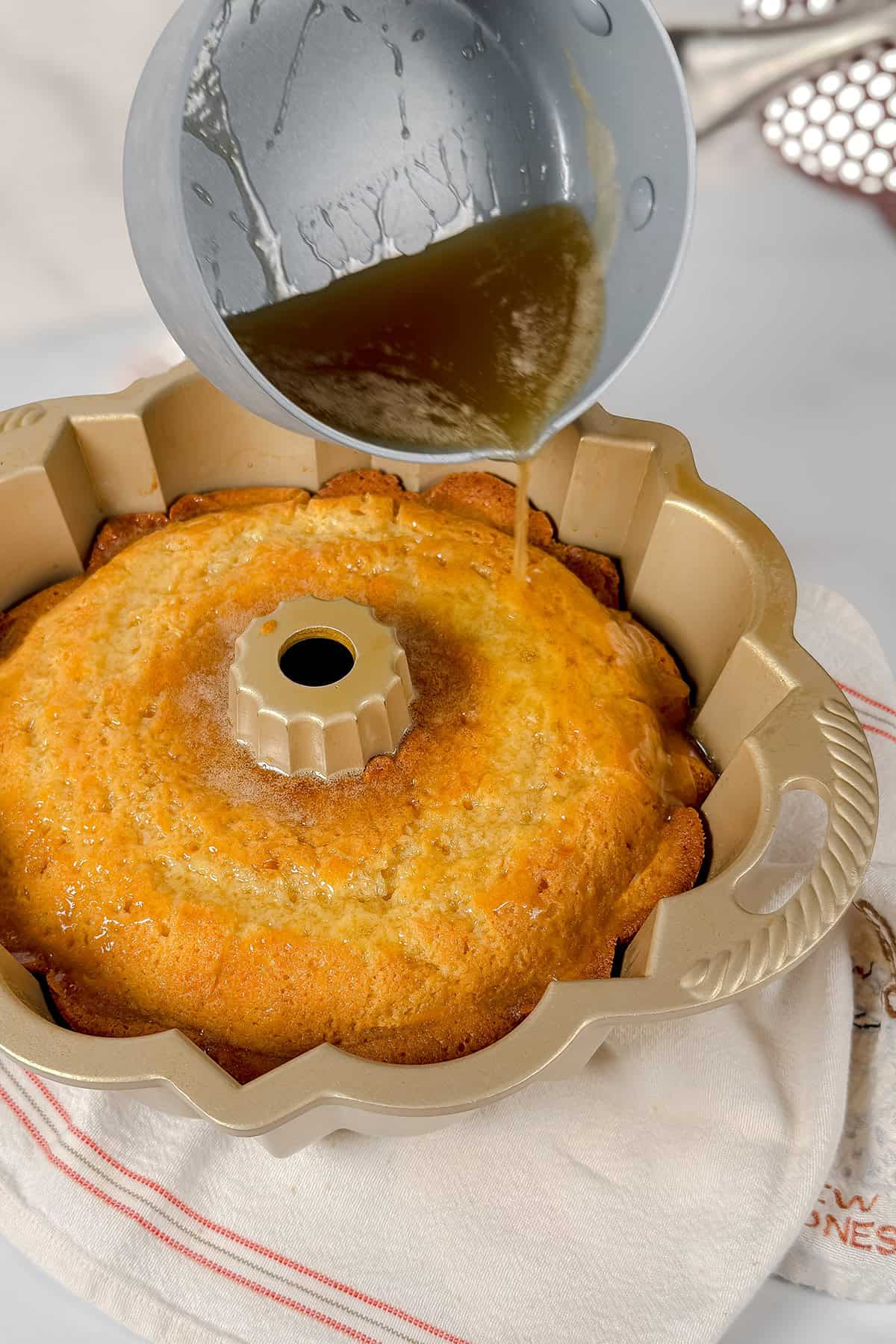 A saucepan pours butter syrup over a freshly baked Kentucky Butter Cake in a Bundt pan.