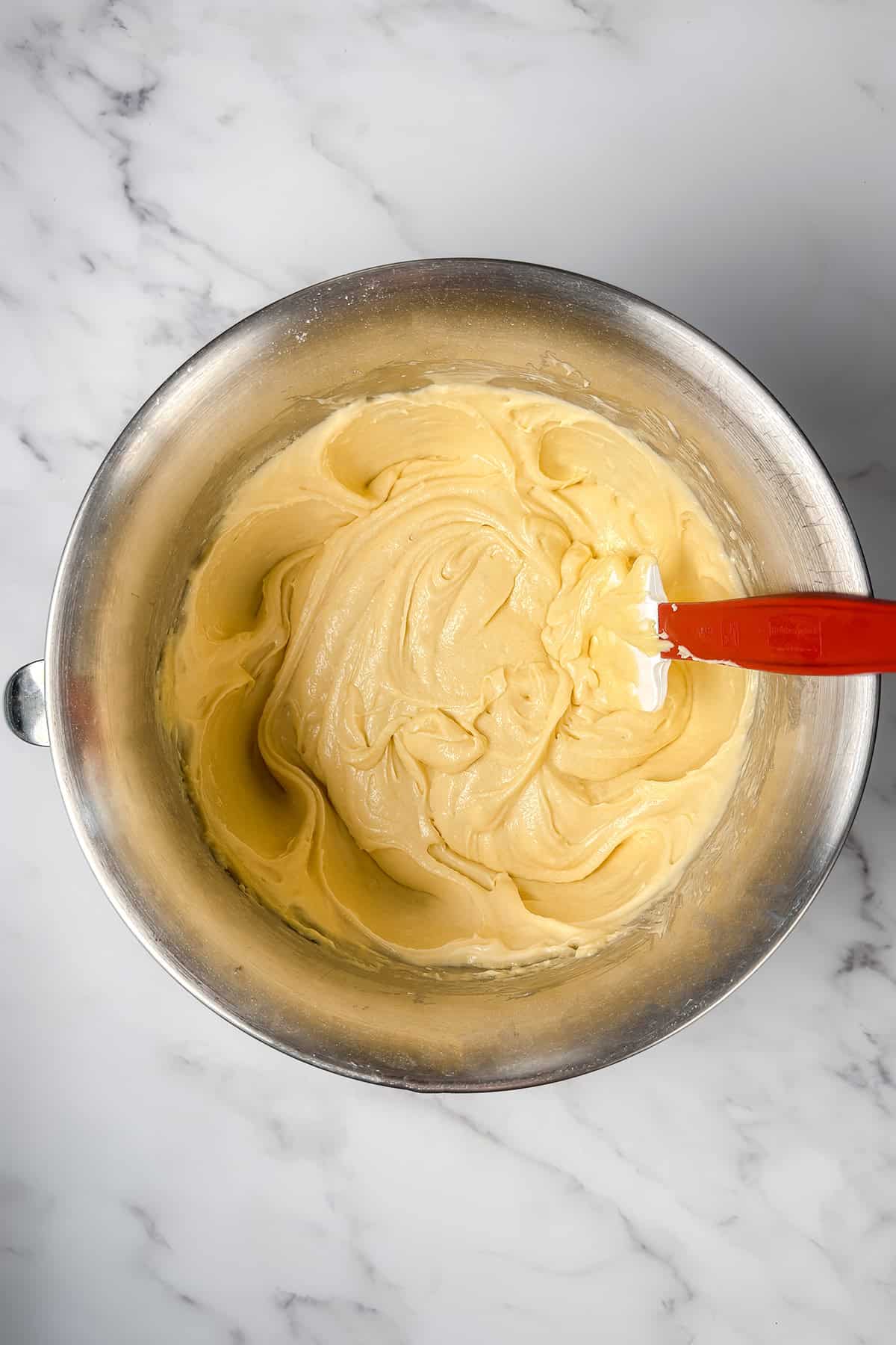 A metal mixing bowl with Kentucky Butter Cake batter and a spatula resting inside.