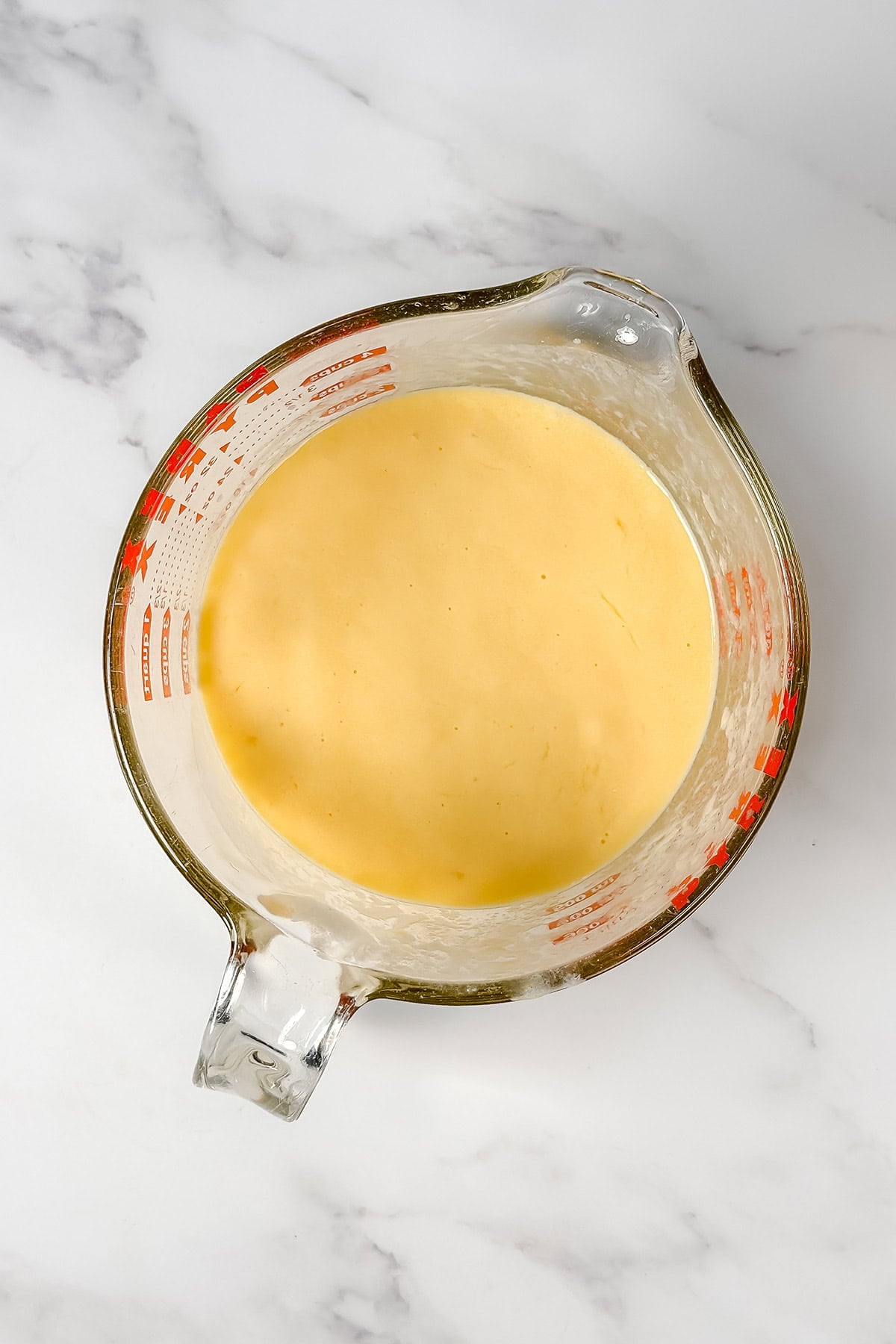 A glass measuring cup filled with creamy Kentucky Butter Cake wet ingredients.