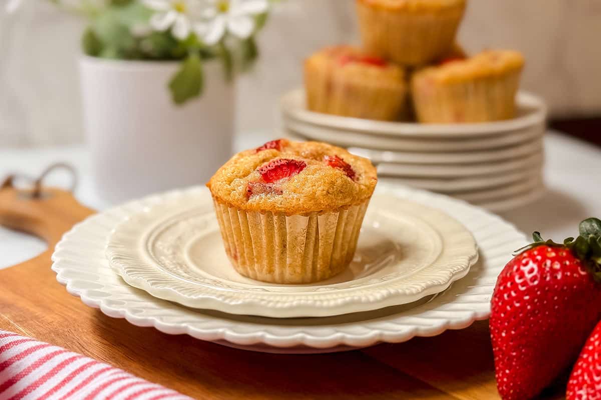 A strawberry muffin on a stack of white plates, with fresh strawberries and more delicious strawberry muffins in the background.