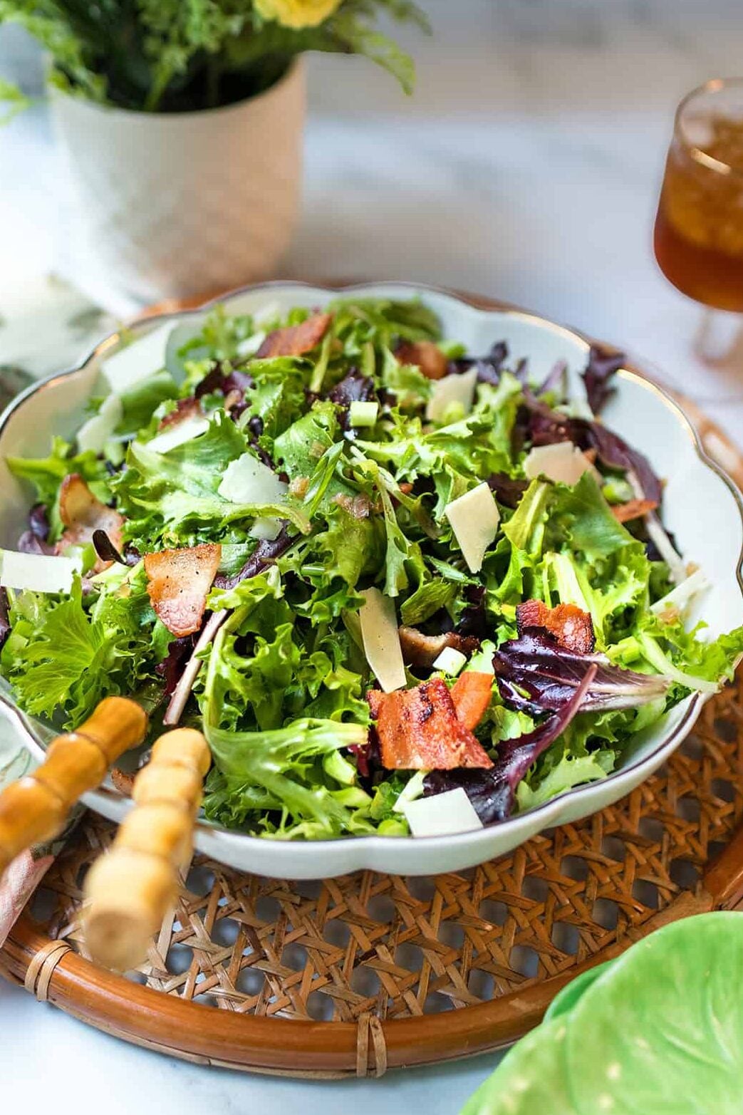 A bowl of spinach and spring green salad, features bacon pieces and shaved Parmesan.