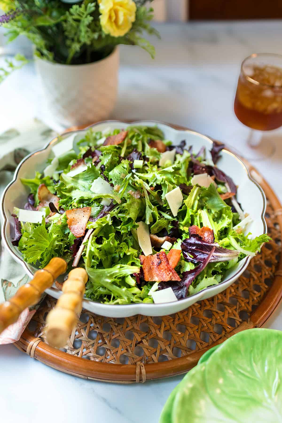 A bowl of spinach and spring green salad, features bacon pieces and shaved Parmesan.