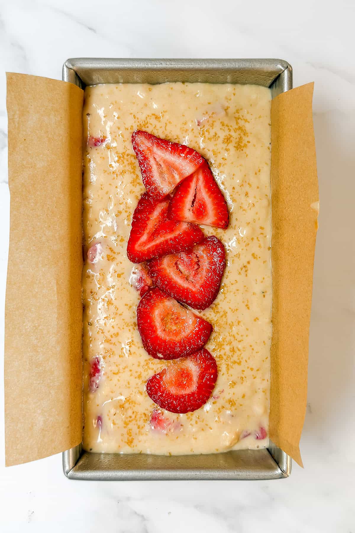 Unbaked loaf of strawberry bread batter in a parchment-lined pan, topped with sliced strawberries and sprinkled with sugar-an inviting sight for any Feast Recipe Template.