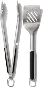 A pair of metal kitchen tongs and a metal slotted spatula with black handles are shown side by side on a white background—perfect tools for preparing your favorite salad recipes.