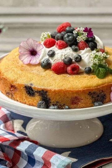 Side view of unsliced berry cake on a white cake stand.