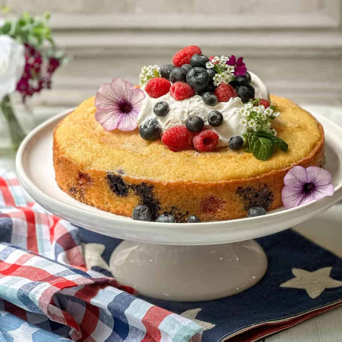 Side view of unsliced berry cake on a white cake stand.