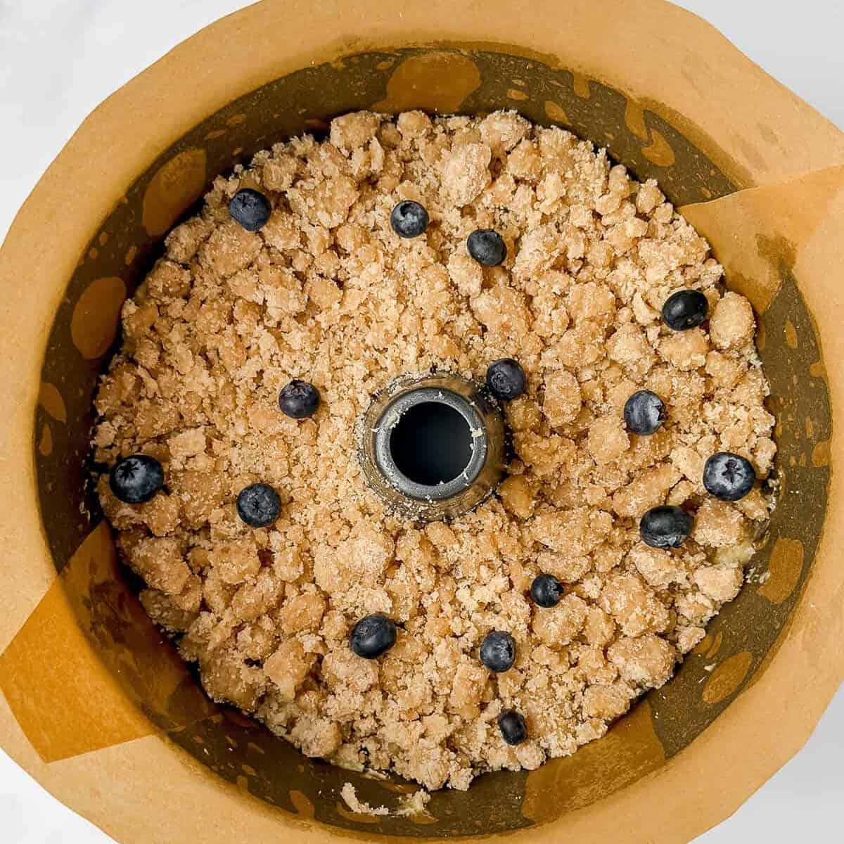 A parchment-lined bundt pan filled with crumbly streusel topping and juicy blueberries, this blueberry teacake is ready to be baked.
