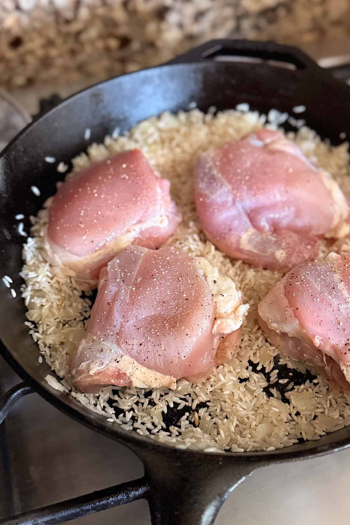 Raw chicken thighs are placed on seasoned white rice in a cast iron skillet, creating a simple one pan chicken and rice dinner.