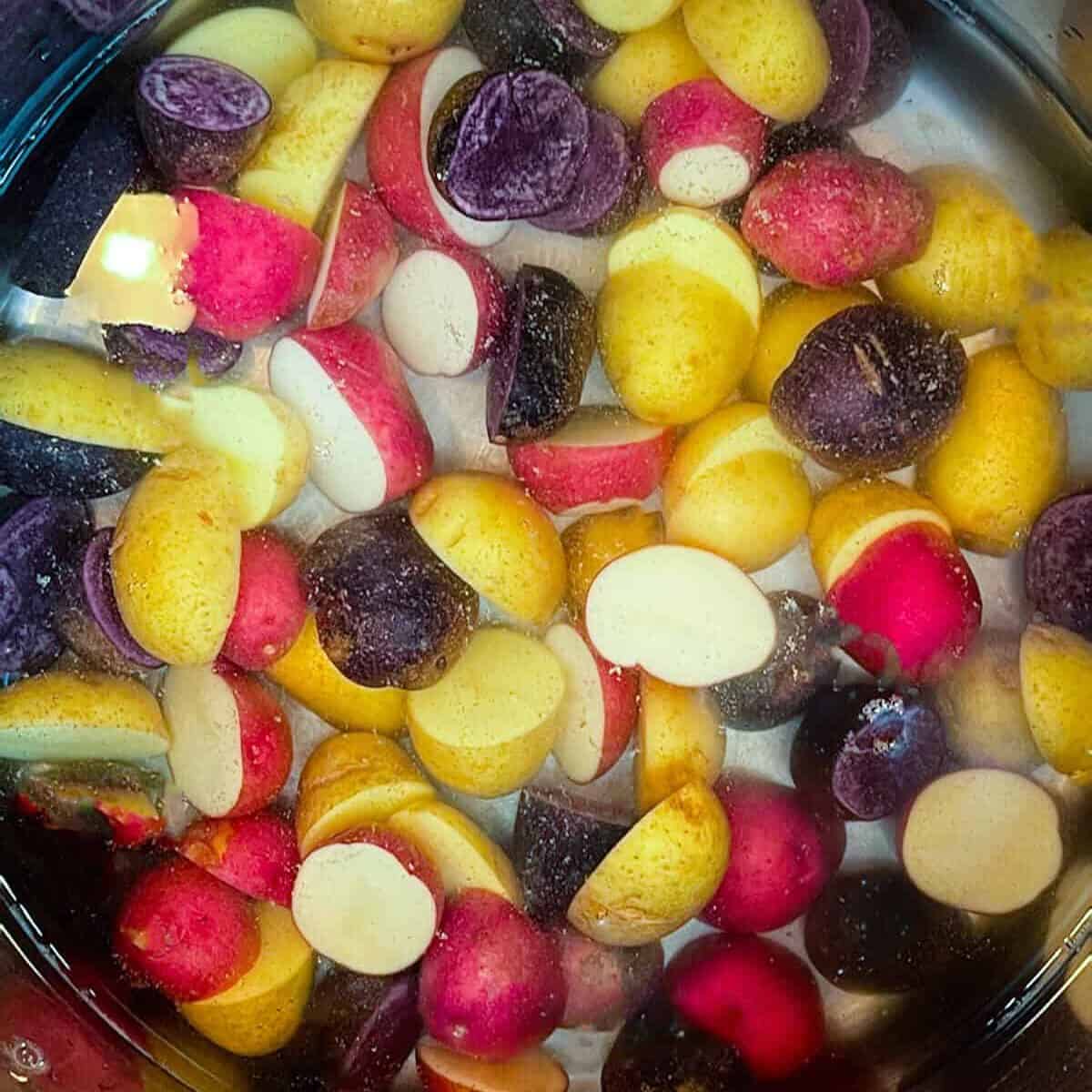 A pot filled with water and a mixture of halved yellow, red, and purple potatoes, perfect for preparing a classic German Potato Salad.