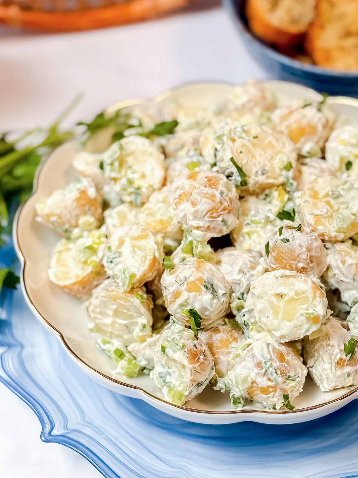 A plate of creamy Yukon Gold potato salad garnished with chopped herbs is displayed on a white dish.