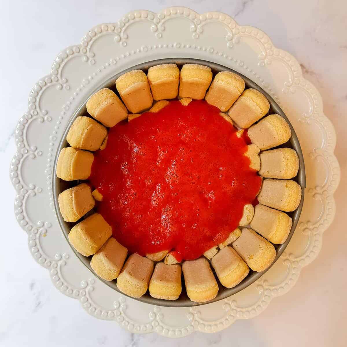 Strawberry sauce spread over a ladyfinger base for a no-bake Strawberry Lady Charlotte Cake.