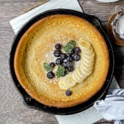 A perfect Father's Day Breakfast: a baked pancake in a cast iron skillet, topped with sliced bananas, blueberries, fresh mint leaves, and a dusting of powdered sugar.