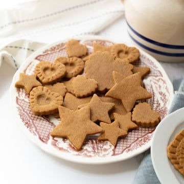 A plate of assorted gingerbread cookies, inspired by a Colonial Williamsburg 1796 recipe, in star, heart, and flower shapes sits on a patterned dish beside a folded napkin.