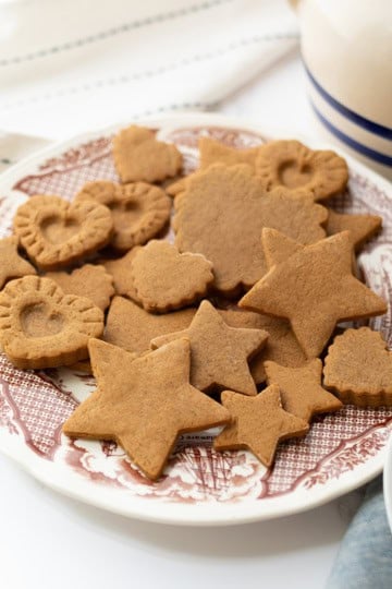 A plate of assorted gingerbread cookies, inspired by a Colonial Williamsburg 1796 recipe, in star, heart, and flower shapes sits on a patterned dish beside a folded napkin.