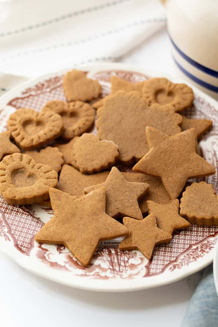 A plate of assorted gingerbread cookies, inspired by a Colonial Williamsburg 1796 recipe, in star, heart, and flower shapes sits on a patterned dish beside a folded napkin.