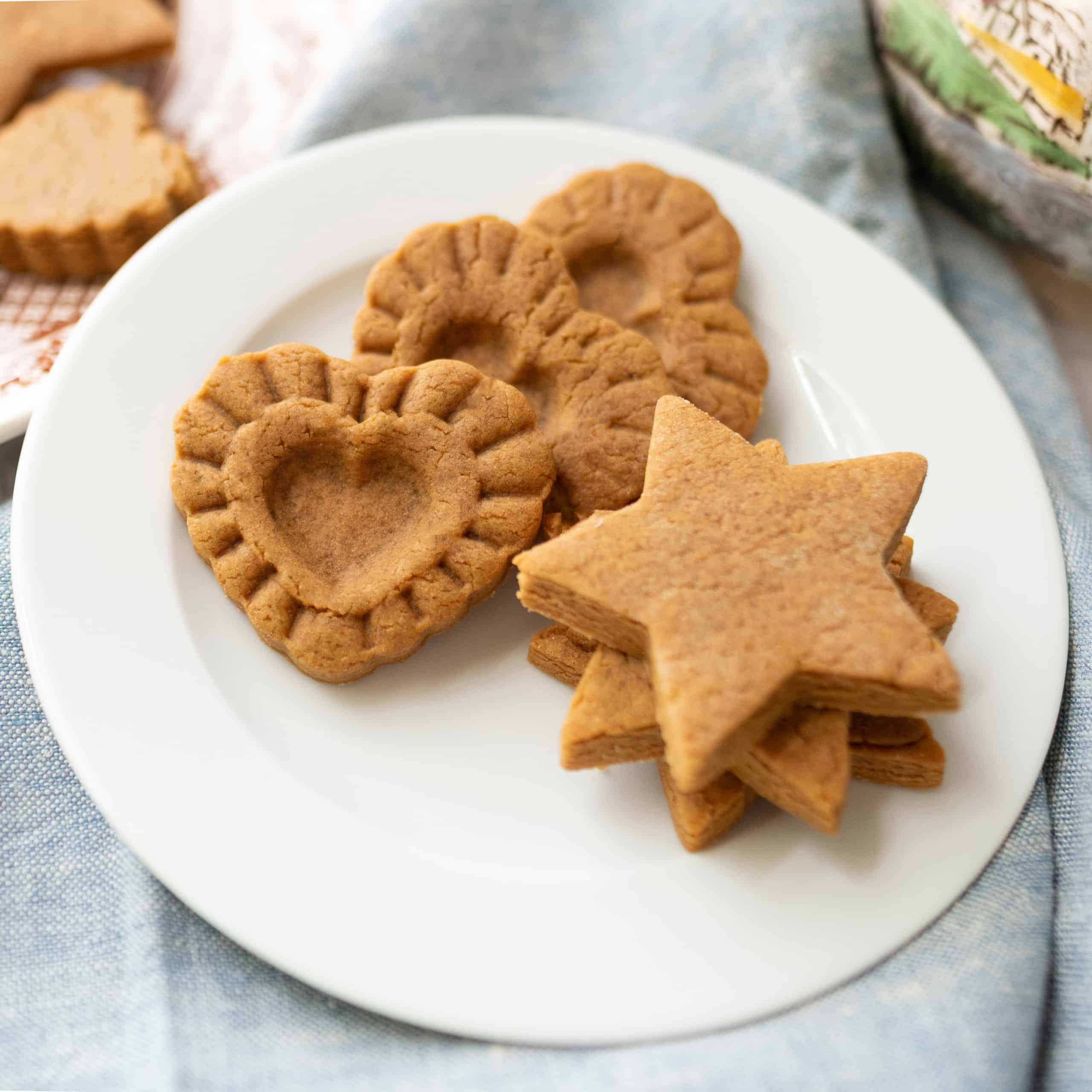 A white plate with heart-shaped and star-shaped gingerbread cookies, inspired by a 1796 recipe from Colonial Williamsburg, rests on a light blue cloth.